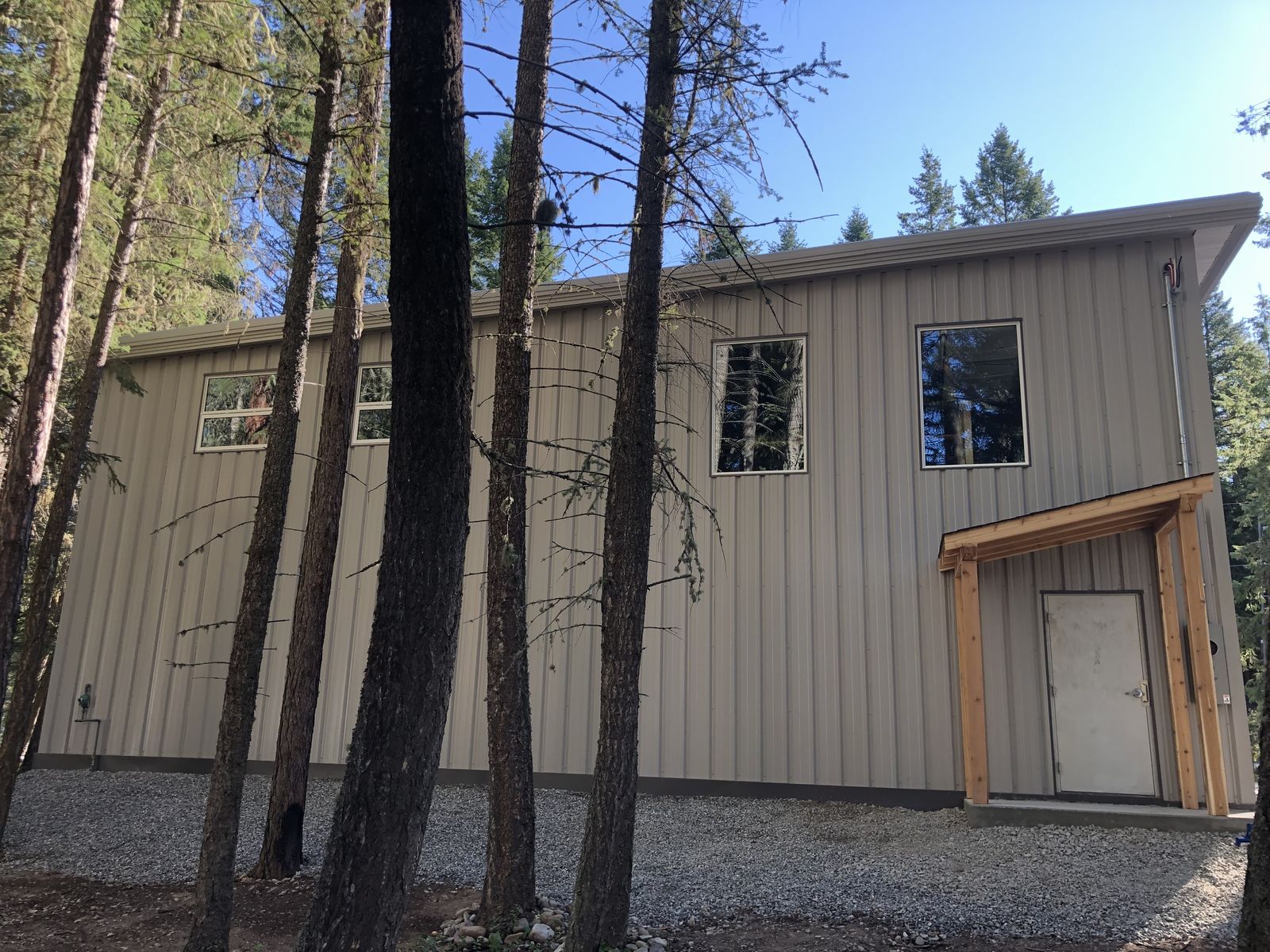 Tall grey steel shop with a timber entry porch in a treed yard