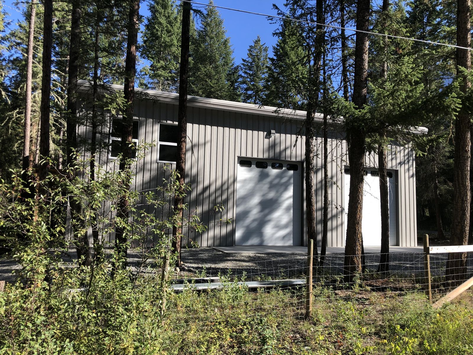 Grey steel shop with an overhead door among tall evergreen trees