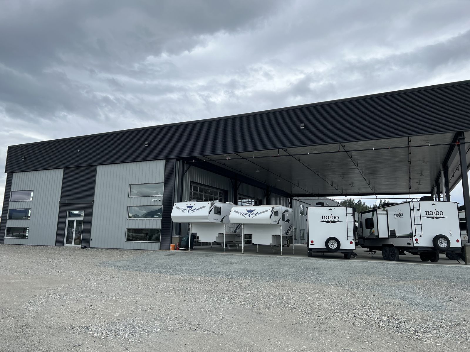 Grey steel building with a large covered canopy and RVs parked underneath