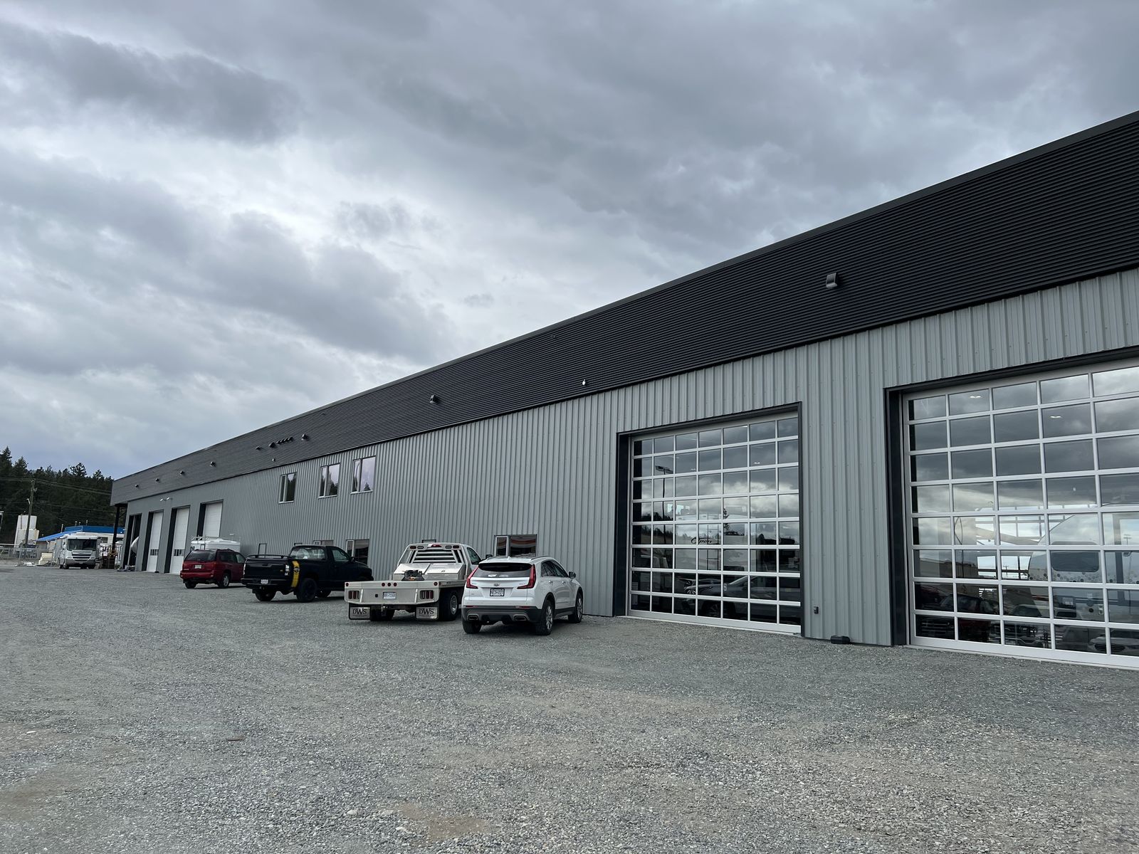 Long grey steel building with glass overhead doors and vehicles parked out front