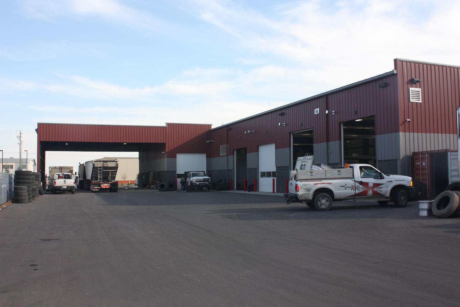 Red and grey steel shop with a drive-through canopy and service trucks parked in front
