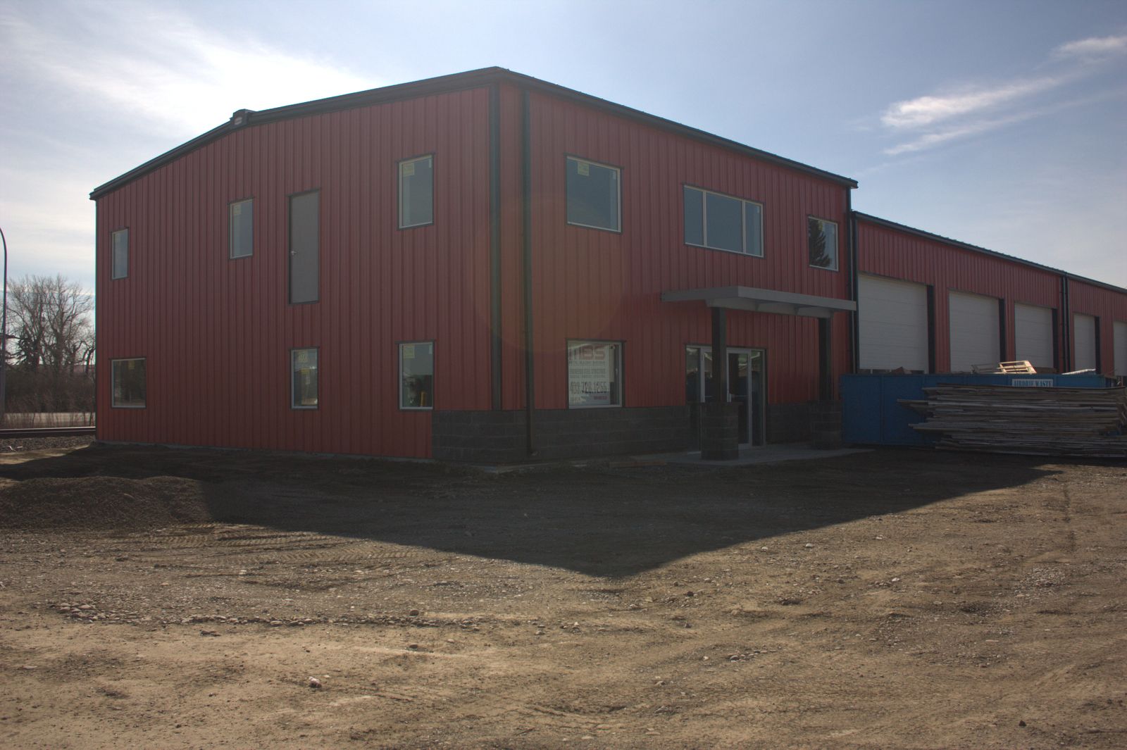 Red two-storey steel building seen from the corner on a gravel lot
